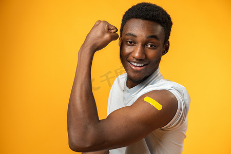 疾病预防背景摄影照片_接种疫苗的非洲裔美国人在黄色背景下展示他的手臂