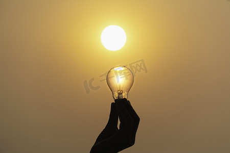 手握日落背景上的灯泡，以节省能源