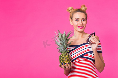 快乐的年轻女人拿着一个菠萝，背景是粉红色的，有复制空间。