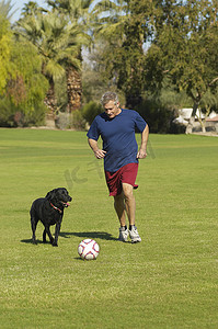 男人和宠物摄影照片_活跃的老人在公园里和狗踢足球