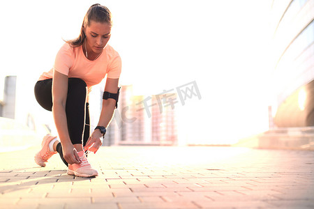年轻健身迷人的运动型女跑步者将鞋带绑在她准备跑步的运动鞋上