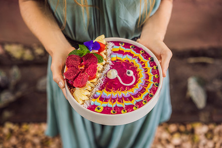 年轻女人吃地中海早餐，吃健康的热带早餐，冰沙碗和热带水果，装饰着彩色酸奶、姜黄和螺旋藻的图案。
