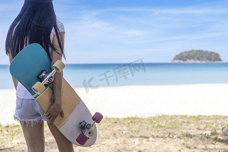 年轻女性拿着有海滩背景的冲浪滑板。