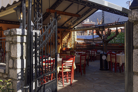 阿凡提卡通摄影照片_有椅子和桌子的希腊空荡荡的小酒馆庭院。