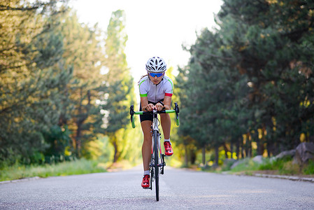 炎热的夏日，年轻女子自行车手在森林的自由道路上骑公路自行车。