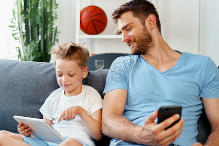 小男孩和他爸爸一起坐在沙发上看数字平板电脑上的视频