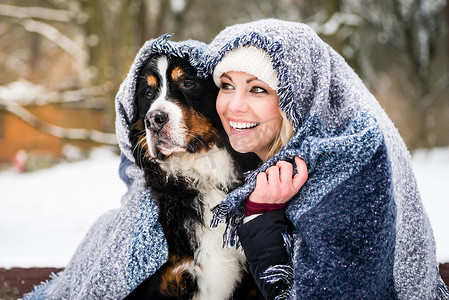 女人和她的狗在寒冷的冬日在毯子下取暖