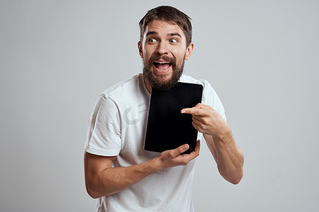 手拿平板摄影照片_手拿平板电脑的情绪化男人触摸屏新技术浅色背景裁剪视图复制空间