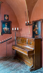 旧木钢琴矗立在红墙的角落里，周围是古老的烛台