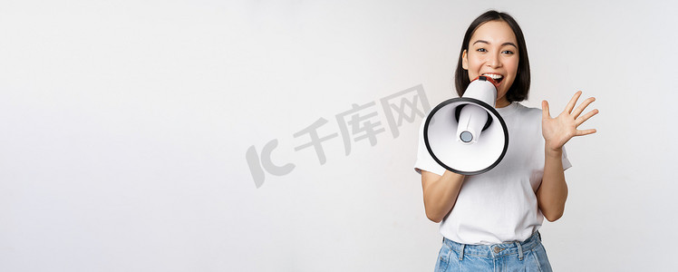 时尚发布摄影照片_快乐的亚洲女人对着扩音器大喊大叫，发布公告，做广告，站在白色背景上