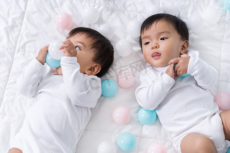 双胞胎婴儿摄影照片_快乐的双胞胎婴儿在床上玩彩球