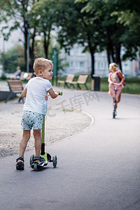 阳光明媚的夏日，穿着时尚短裤的帅气小男孩在公园的跑道上骑着摩托车