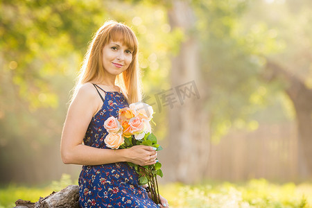 绿色暖色调摄影照片_美丽的年轻女子，在绿色阳光模糊的背景下，手里拿着一束玫瑰