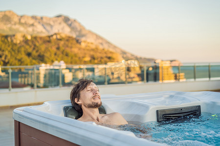 绿色大山背景下享受快乐旅行时光度假生活时，年轻无忧无虑的快乐微笑男子在热水浴缸中放松的肖像