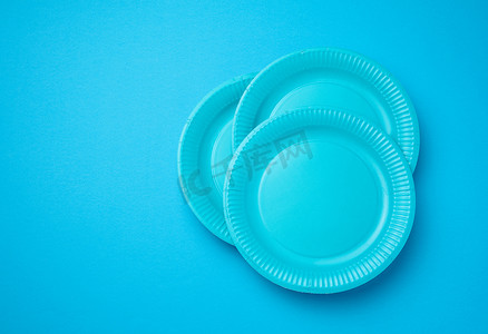 餐具包装摄影照片_蓝色背景上的空白皮书一次性盘子，顶视图。