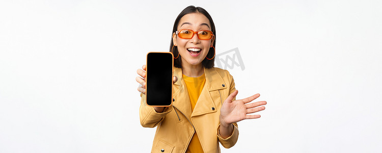 热情的亚洲女模特，在手机屏幕上展示智能手机应用程序界面、在线商店或网站，站在白色背景上