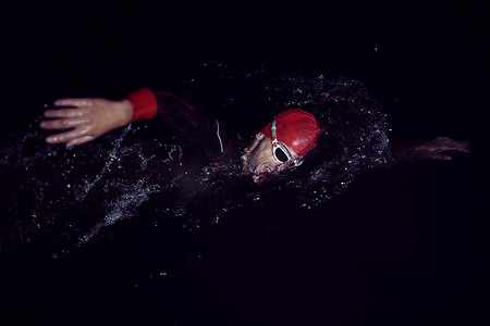 漆黑的夜晚摄影照片_铁人三项运动员穿着潜水服在漆黑的夜晚游泳