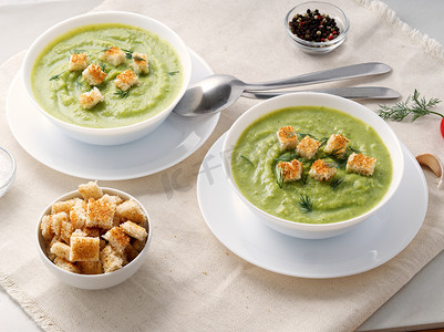 两个大白碗，白色背景，侧视，配有西兰花、西葫芦、绿豌豆蔬菜绿色奶油汤