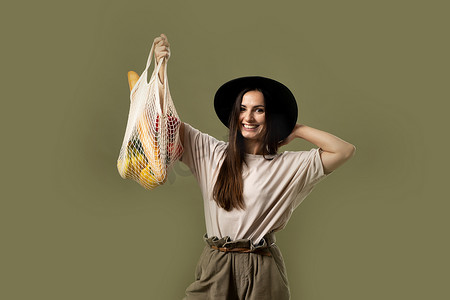 女人带着网眼生态袋，里面装着蔬菜、蔬菜和水果，没有塑料袋。