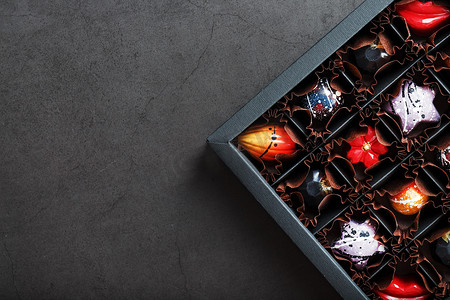 一套五颜六色的独家手工巧克力，放在黑色背景的盒子里。