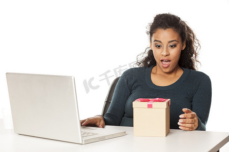 办公桌前拿着笔记本电脑的非洲女人打开一个装有礼物的盒子
