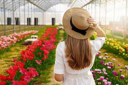 美丽的女孩拿着草帽走在花间，准备在日落时野餐。