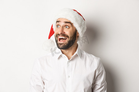 商打折促销海报摄影照片_特写：戴着圣诞帽、留着胡子的男人，兴奋地向左看，圣诞节促销优惠，站在白色背景上