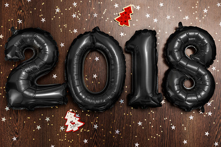 年摄影照片_明亮的金属黑色气球人物2018年、圣诞节、新年气球，深色木桌背景上有闪闪发光的星星