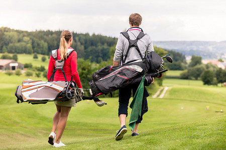 高尔夫球包摄影照片_夫妇背着高尔夫球包的后视图