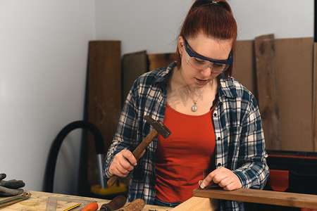 年轻的红发女人，木匠在她的小木工店里将钉子钉入木板。