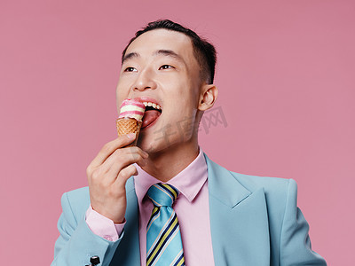 韩国经典摄影照片_穿着蓝色经典西装、在粉红色背景中吃冰淇淋的快乐亚洲男人