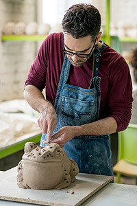 穿着围裙的陶艺家在明亮的陶瓷工作室用生粘土雕刻雕像。