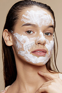 年轻女子面罩霜清洁皮肤面部磨砂米色背景