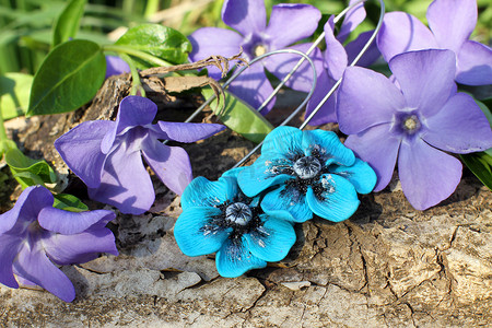 蓝紫色吊坠摄影照片_自然背景下手工制作的蓝花粘土耳环