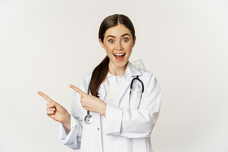 微笑的年轻女医生、医疗保健医务工作者的肖像，手指向左，展示诊所促销、标志或横幅，站在白色背景上