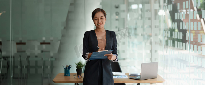 使用笔记本电脑和计算器进行财务会计工作时，自信的亚洲女商人站立着