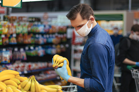 戴防护手套的顾客在超市挑选香蕉