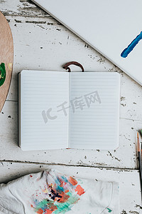 带笔记本的平刷在白色木质背景上用空白空间和油漆调色板做笔记。