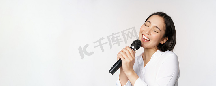 站在白色背景上的亚洲女性在卡拉 OK 用麦克风唱歌的特写