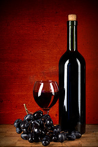 红色垃圾背景下的一瓶酒、玻璃和葡萄