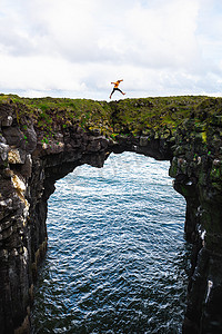 游客跳过冰岛阿尔纳斯塔皮的一座天然石桥