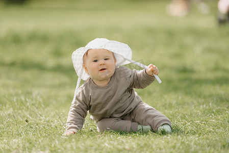 一个戴着白色巴拿马草帽的 7 个月大的孩子在草地上玩得很开心。
