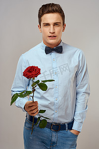 浪漫的男人，戴着红玫瑰，身穿蓝色衬衫，脖子上系着领结，灰色背景