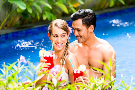 亚洲比基尼摄影照片_亚洲酒店泳池里的情侣喝鸡尾酒