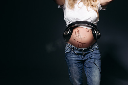 肚子上戴着大耳机的时尚怀孕妈妈的作物。