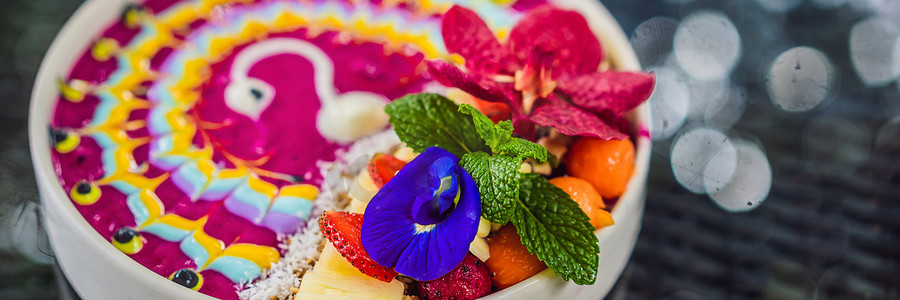 水果图案装饰摄影照片_横幅，长格式健康热带早餐，热带水果冰沙碗，装饰着五颜六色的酸奶与姜黄和螺旋藻的图案。