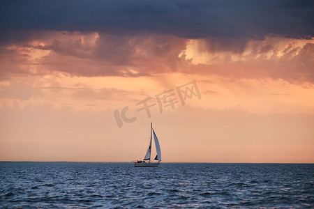 天空背景摄影照片_孤单的帆船出海，粉红色的天空，暴风雨的天空