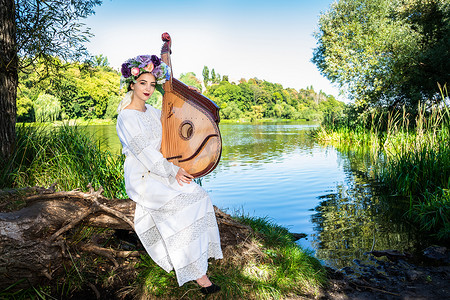 一位身着民族服饰、头戴花环的乌克兰年轻女子坐在河边，手里拿着班杜拉