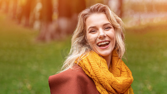 身着秋装和黄色针织围巾的快乐的年轻女子站在秋天的黄色花园或公园里快乐地微笑着。