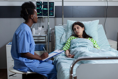 护士坐在病人床边，在日常就诊咨询妇女时用病历在剪贴板上写字